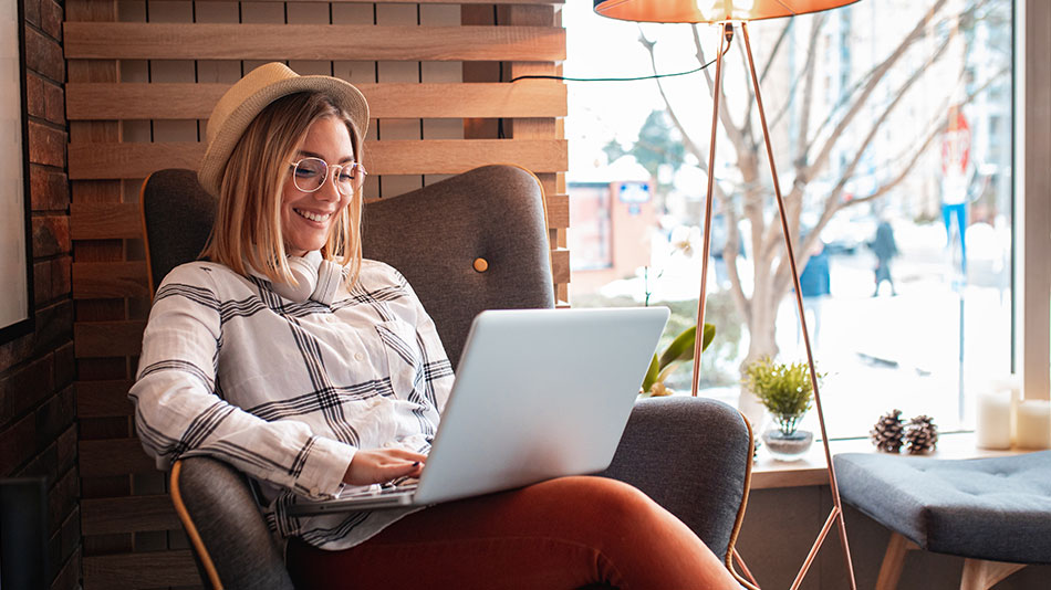 A woman sits by the window in the cafe, working on her laptop.