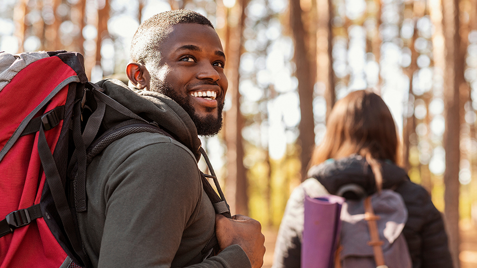 An amazed man with a red backpack marvels at nature while hiking.